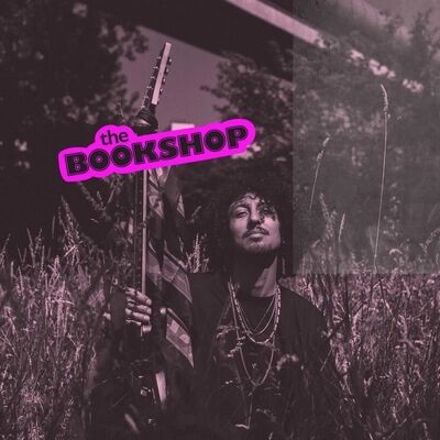 Beeld bij Nosebleed Blues: een paars getinte foto van een muzikant met krullend haar die een gitaar rechtop naast zich houdt, staand in hoog gras. Linksboven staat het roze logo 'the BOOKSHOP'.